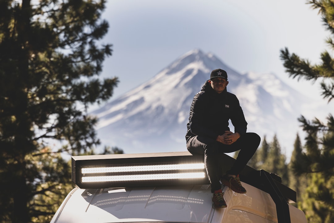 a man sitting on top of a car in front of a mountain