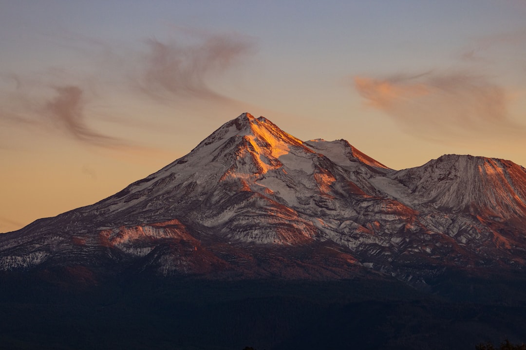 a snow covered mountain at sunset with clouds in the sky